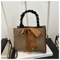 Close-up of brown handbag featuring a black woven handle and a large ribbon bow decoration - Brown
