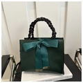 Detail of dark green handbag featuring large cyan satin bow and black braided handle - Green