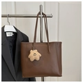 Close-up of a brown leather tote bag with fine stitching and a cute plush bear charm - With Charm / Brown