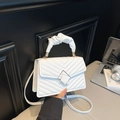 White quilted leather handbag with ruched handle and geometric metal lock on a desk - White