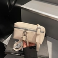 Minimalist beige square crossbody bag with metallic robot charm on grey interior backdrop - Off White