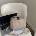 Bolso bandolera beige minimalista estilo concha con cremallera doble en silla blanca - Caqui
