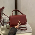 Bolso burdeos brillante con cierre en A dorado presentado en un ambiente de estilo de vida - Rojo