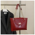 Detail of red glossy tote bag featuring a silver deer charm and gold chain strap - Red