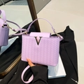 Light purple textured woven crossbody bag with gold V-buckle on black background - Purple