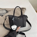 Black nylon mini tote bag with adjustable strap and cute panda charm on a beige jacket - Black