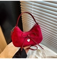 Close-up of red suede hobo bag with delicate bow and silver heart pendant detail - Red