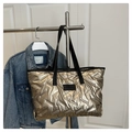 Detail der champagnergoldenen Stepptasche mit Metallic-Finish und schwarzen Schultergurten - Gold