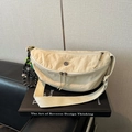 Detail van de crèmewitte nylon crossbodytas in halve maanvorm op een leren bank - Wit Met Hanger