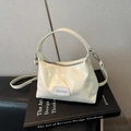 Minimalist beige glossy patent leather handbag with adjustable strap on a book - Cream