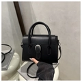 Close-up of matte black crossbody bag with silver horseshoe buckle on white stand - Black