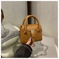 Mini-Handtasche in Hellbraun mit Silberkette und Zierschnalle auf einem Buchhintergrund - Braun