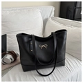 Close-up of black tote bag featuring a golden metal bow and elegant rivet details - Black