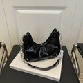 Bolso hobo de charol negro con cadena plateada sobre un libro blanco - Negro