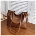 Detail of a brown leather tote bag with a fashion label on a wooden surface - Brown
