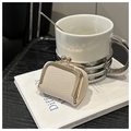 Détail du mini sac à bijoux crème texture litchi avec fermoir doré sur un livre - Blanc