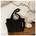 Detalle de bolso tote de pana negra con bolsillo lateral y detalle de borla blanca - Negro