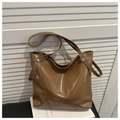 Close-up of brown glossy leather tote bag with vertical stitching and metal rivet details - Brown
