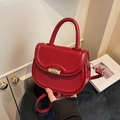 Minimalist deep red leather shoulder bag with gold metal clasp on a textured surface - Red