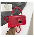 Detail of red crocodile texture flap handbag with a gold geometric clasp on a grey blazer - Red
