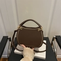 Brown leather crossbody bag with gold zipper trim and round handle on white book - Brown