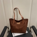 Dark brown faux suede tote bag with FASHION leather patch placed on a chair - Red Brown