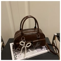 Brown gloss Boston bag with pearl bow charm and dual front pockets on a black chair - Brown