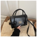 Detail der schwarzen Handtasche mit goldener Logo-Plakette auf beigem Strickkissen - Schwarz