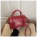 Detail einer roten Kunstlederhandtasche mit goldenem Metallverschluss und Markenlogo - Rot