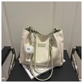 Detail van crème tote bag met groene bies, fashion-label en een witte pluche tashanger aan stoel - Groen met hanger