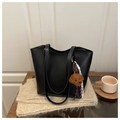 Detail of minimalist black leather tote bag with plush bear charm on wooden table - Black With Pendant