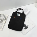 Funda negra para portátil con dos bolsillos y botones de colores en mesa blanca - Estilo Funda Negra para Tableta