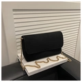 Detail of black suede flap crossbody bag featuring a thick gold chain strap on a book - Black