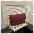 Close-up of burgundy suede flap bag with gold chain strap resting on a white book - Red
