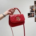 Elegant red quilted crossbody bag with gold M logo, held by hand against a white wall - Red