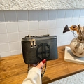 Dark grey box-shaped tote bag with matte texture and gold chain strap held by hand - Black