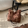 Detail of dark brown suede tote bag with golden metal chains on a white plush rug - Brown