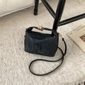 Elegante borsa a tracolla nera testurizzata con fibbia dorata su tappeto bianco - Nero