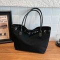 Bolso tote negro de lona con ojales metálicos y correas de cuero sobre madera - Negro