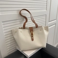Bolso tote de cuero beige con correas marrones y hebilla dorada en un sofá - Blanco