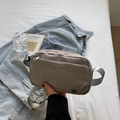 Sac bandoulière en nylon taupe avec plusieurs poches sur un lit blanc avec accessoires - Gris