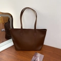 Minimalist deep brown matte leather tote bag with long straps shown on a wooden desk - Brown