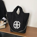 Fuzzy black fleece tote bag with white B logo and striped shoulder strap on a wooden desk - Black