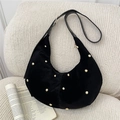 Elegante bolso hobo de terciopelo negro con remaches dorados en un sofá - Negro