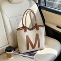 Schicke beige gewebte Tragetasche mit braunem M-Patch aus Leder auf dem Autositz - Weiß