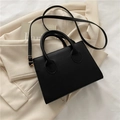 Bolso de mano negro minimalista con asas y correa sobre una chaqueta beige - Negro