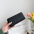 Close-up of black quilted long wallet with golden zipper detail held in hand - Black