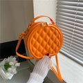 Detailed view of an orange round quilted crossbody bag with gold hardware in a home setting - Orange Red