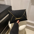 Detail of black quilted envelope clutch bag with elegant gold metal trim being held - Black