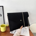 Pochette a busta nera glitterata minimalista con catena dorata su un tavolo di legno - Nero